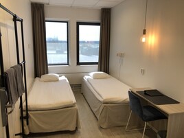 Habitación de hotel con dos camas individuales, un escritorio con silla y vista a un estacionamiento a través de dos ventanas.
