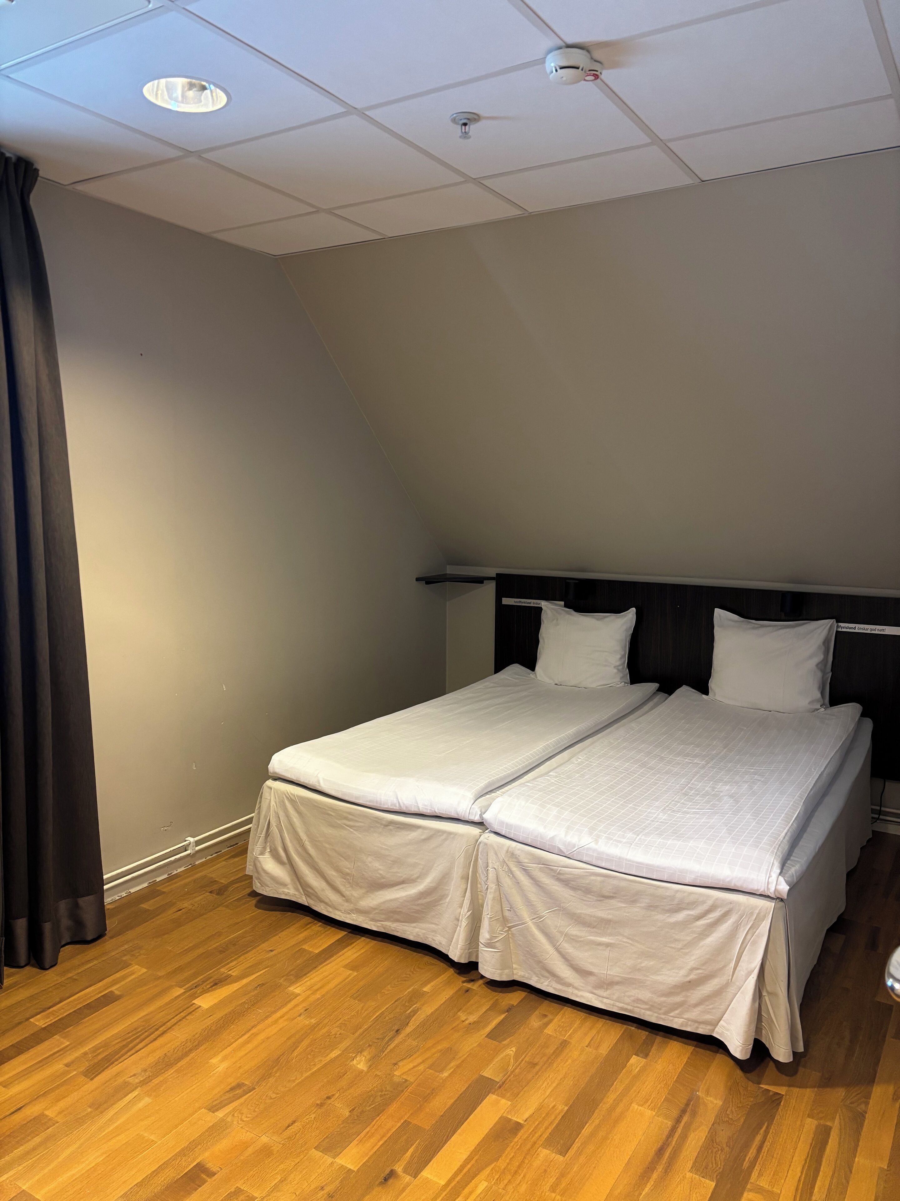 A neatly made bed with a headboard, a wooden floor, and a ceiling with recessed lighting.