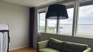 A room with a green sofa, a black table, a window with a view of a building and a body of water, and a ceiling with a grid pattern. - Hotell Fyrislund (Uppsala)