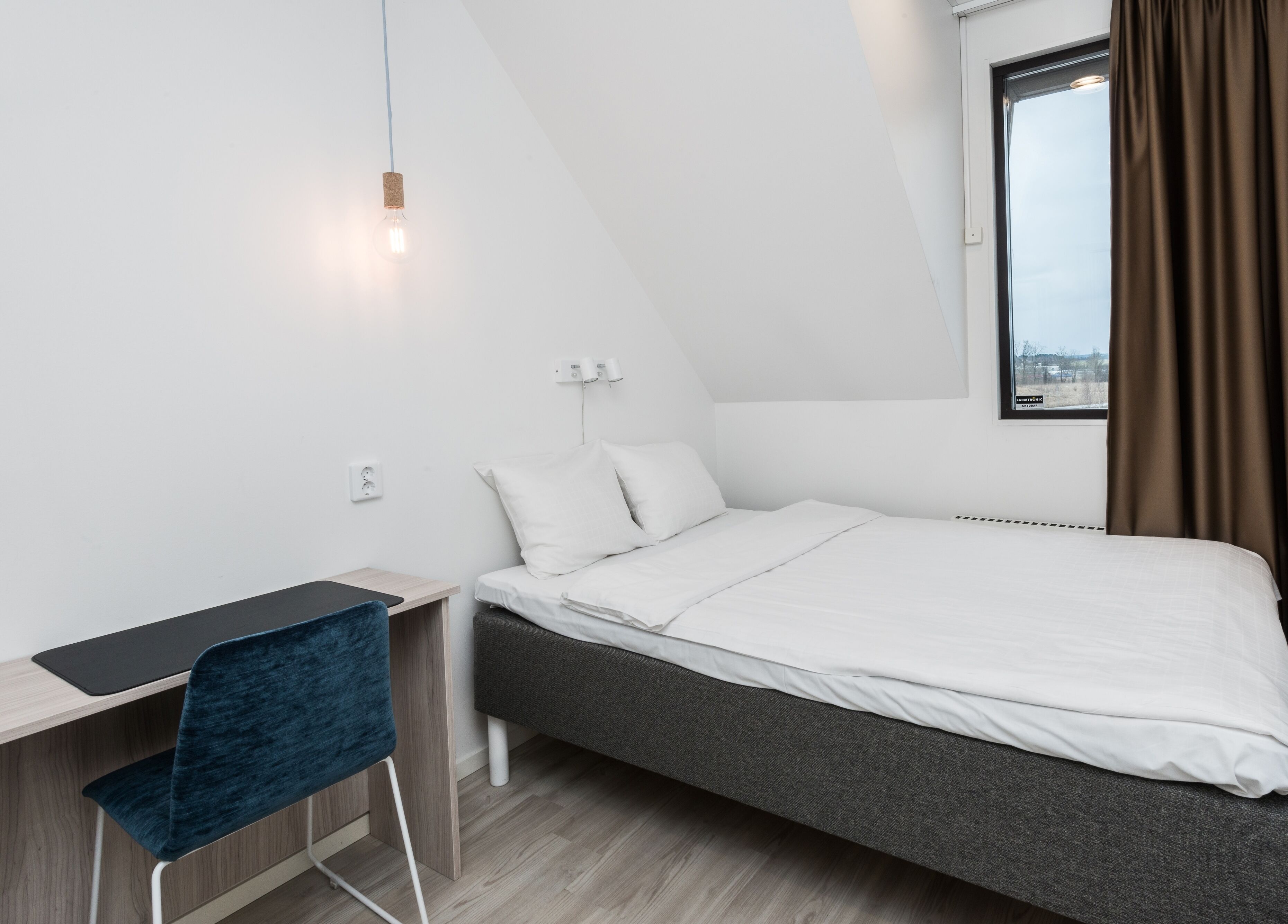 A modern, minimalist bedroom with a single bed, a desk, and a chair.