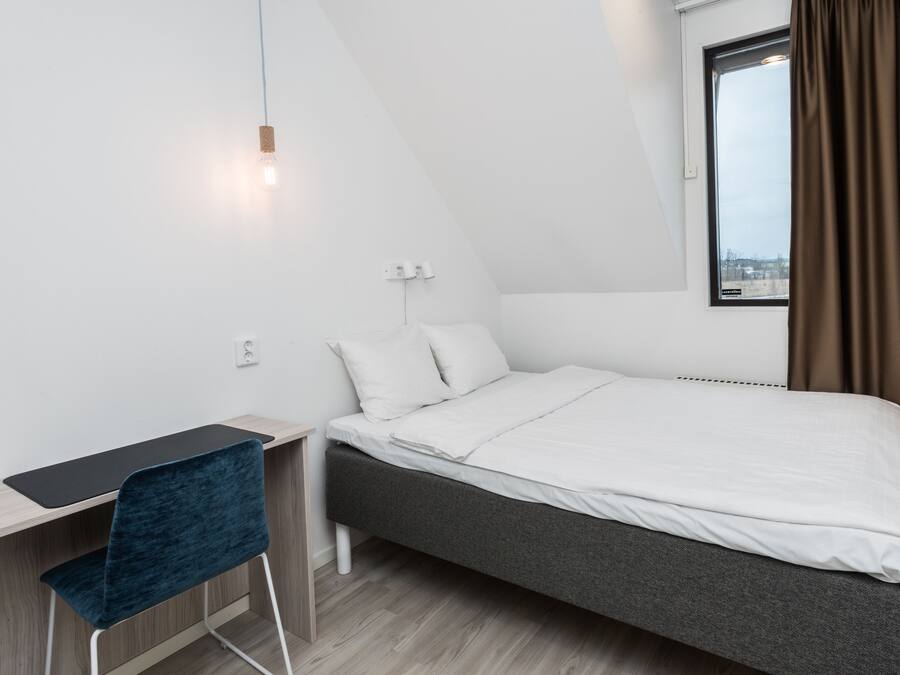A modern, minimalist bedroom with a single bed, a desk, and a chair.