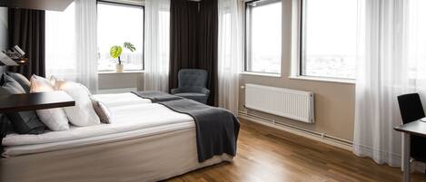 A modern hotel room with a large bed, a chair, a table, and a window with a view.