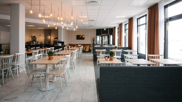 A modern restaurant with high ceilings, pendant lighting, and a mix of seating options including tables and booths. - Hotell Fyrislund (Uppsala)