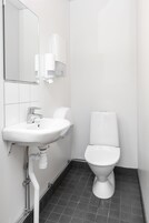 Un baño pequeño y moderno con lavamanos, inodoro e piso de baldosas blancos.