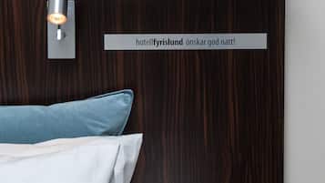 A hotel room with a dark wood headboard, a wall-mounted light fixture, and a sign that reads "hotelfyrlisland önskar god natt!"