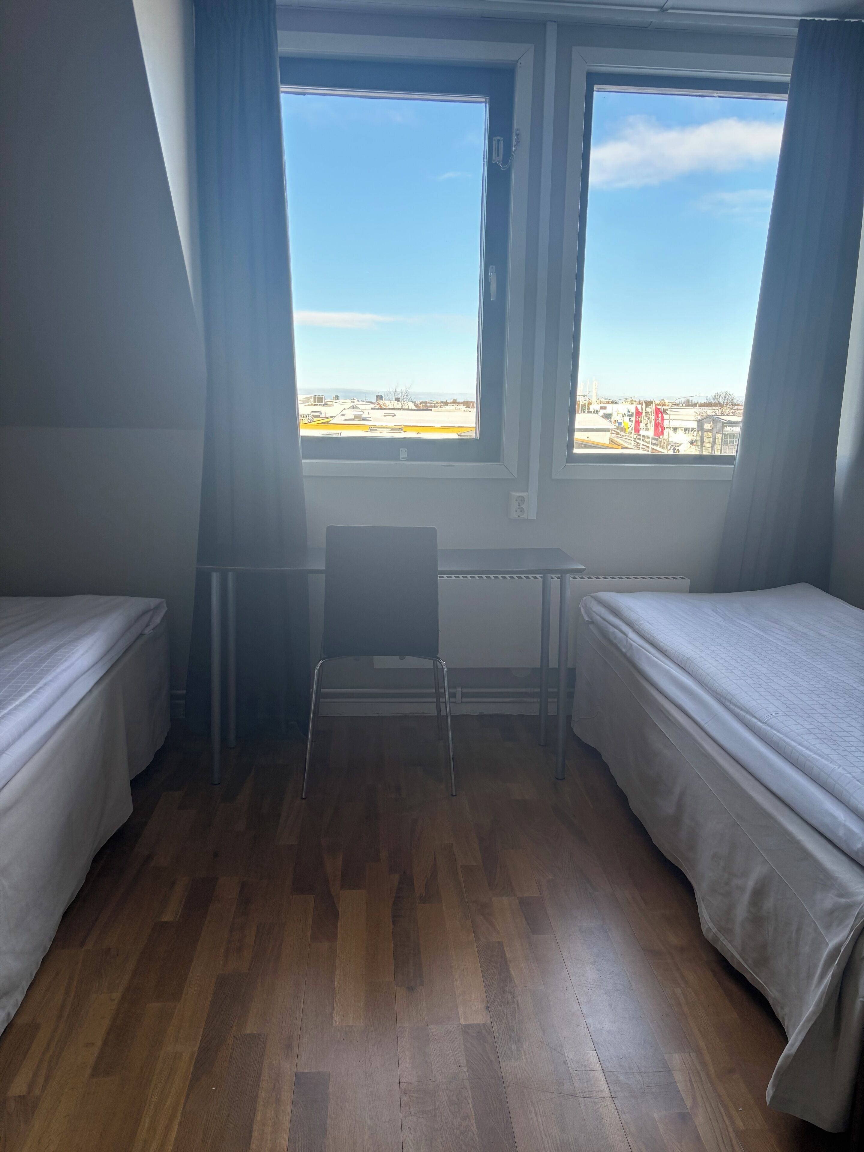 A room with two beds, a chair, and a window with a view of buildings.