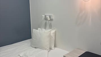 Una cama bien hecha con ropa blanca, una mesita de noche pequeña y una silla azul.