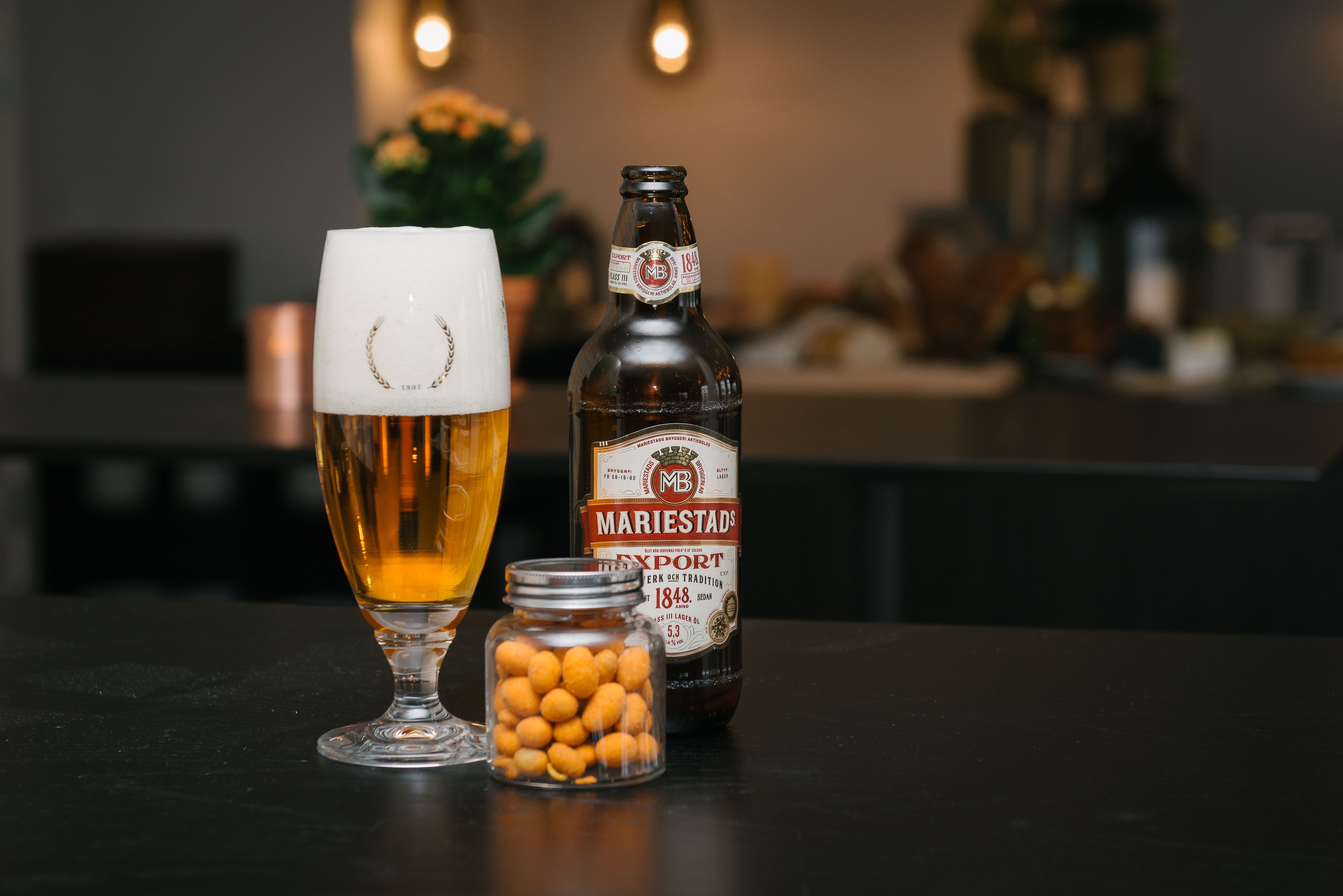 A glass of beer, a bottle of beer, and a jar of snacks on a table.