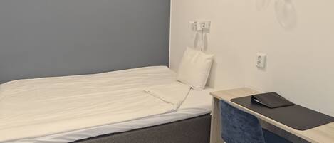 A small, neatly arranged bedroom with a bed, a desk, and a chair.