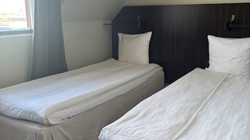 Una habitación con dos camas individuales, piso de madera, ventana con cortinas y cabecero de madera oscura.