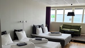 A hotel room with three beds, a green sofa, and a view of the sea. - Hotell Fyrislund (Uppsala)