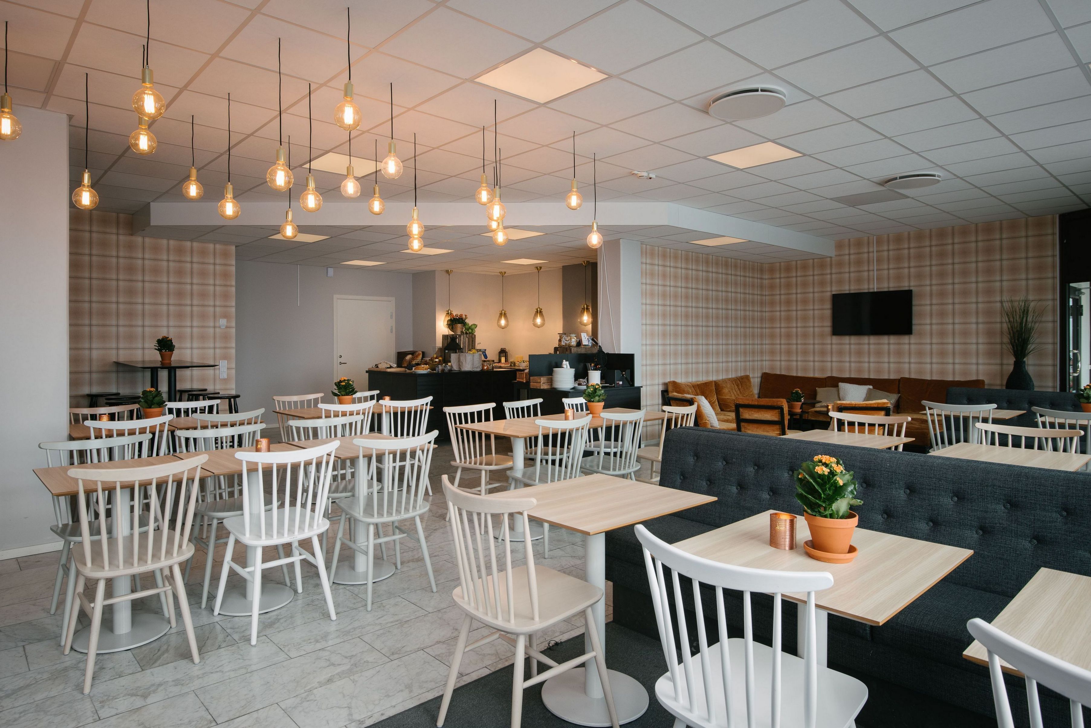 A modern cafe with white chairs and tables, a grey sofa, and hanging pendant lights.