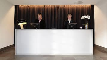 Un mostrador de recepción con dos personas detrás, un telón oscuro de fondo y un diseño de techo moderno.