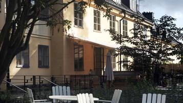 An outdoor seating area with white chairs and tables, surrounded by a building with large windows and a balcony.