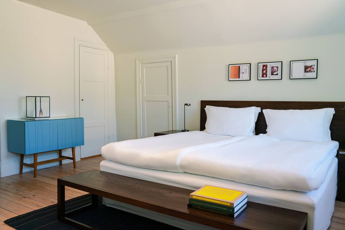 A bedroom with a bed, a bedside table with a book, a blue cabinet, and framed pictures on the wall.