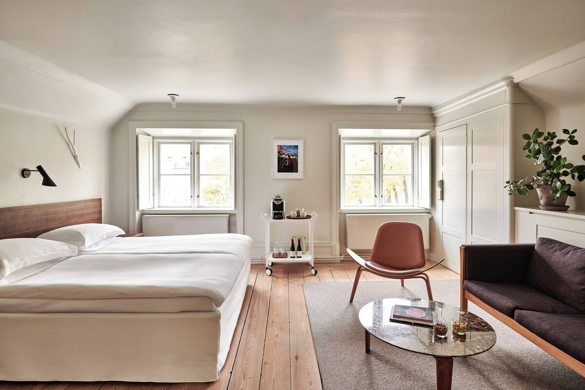 A hotel room with a bed, a chair, a sofa, a small table, and a radiator.