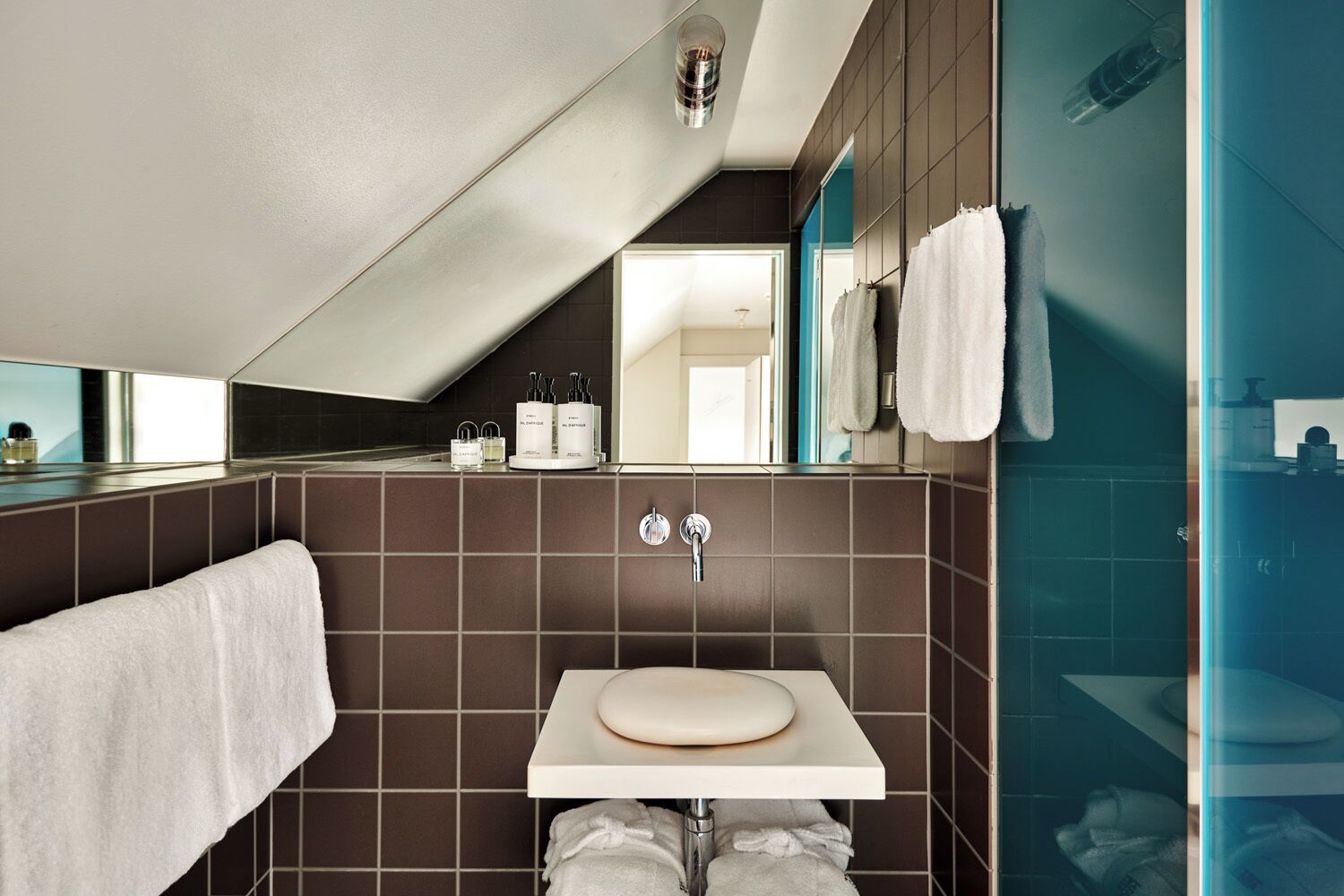 Un baño moderno con techo inclinado, un lavamanos blanco y un espejo grande.