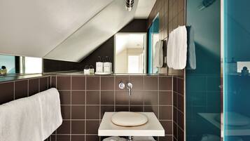 Un baño moderno con techo inclinado, un lavamanos blanco y un espejo grande.