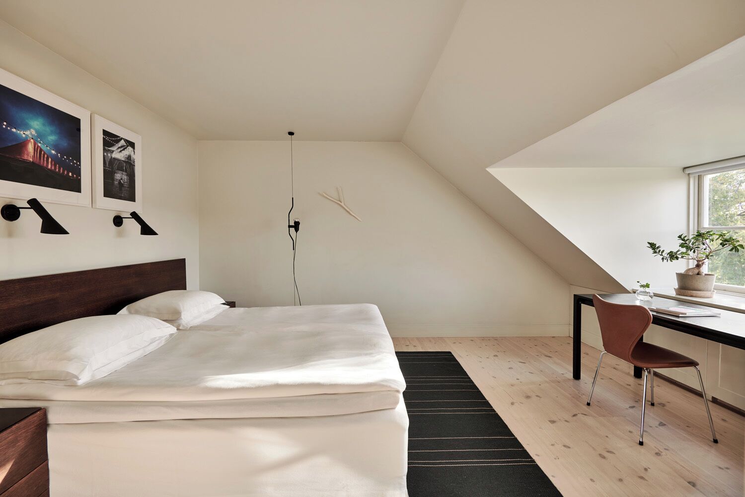 Un dormitorio con cama, escritorio, silla, ventana y una planta.
