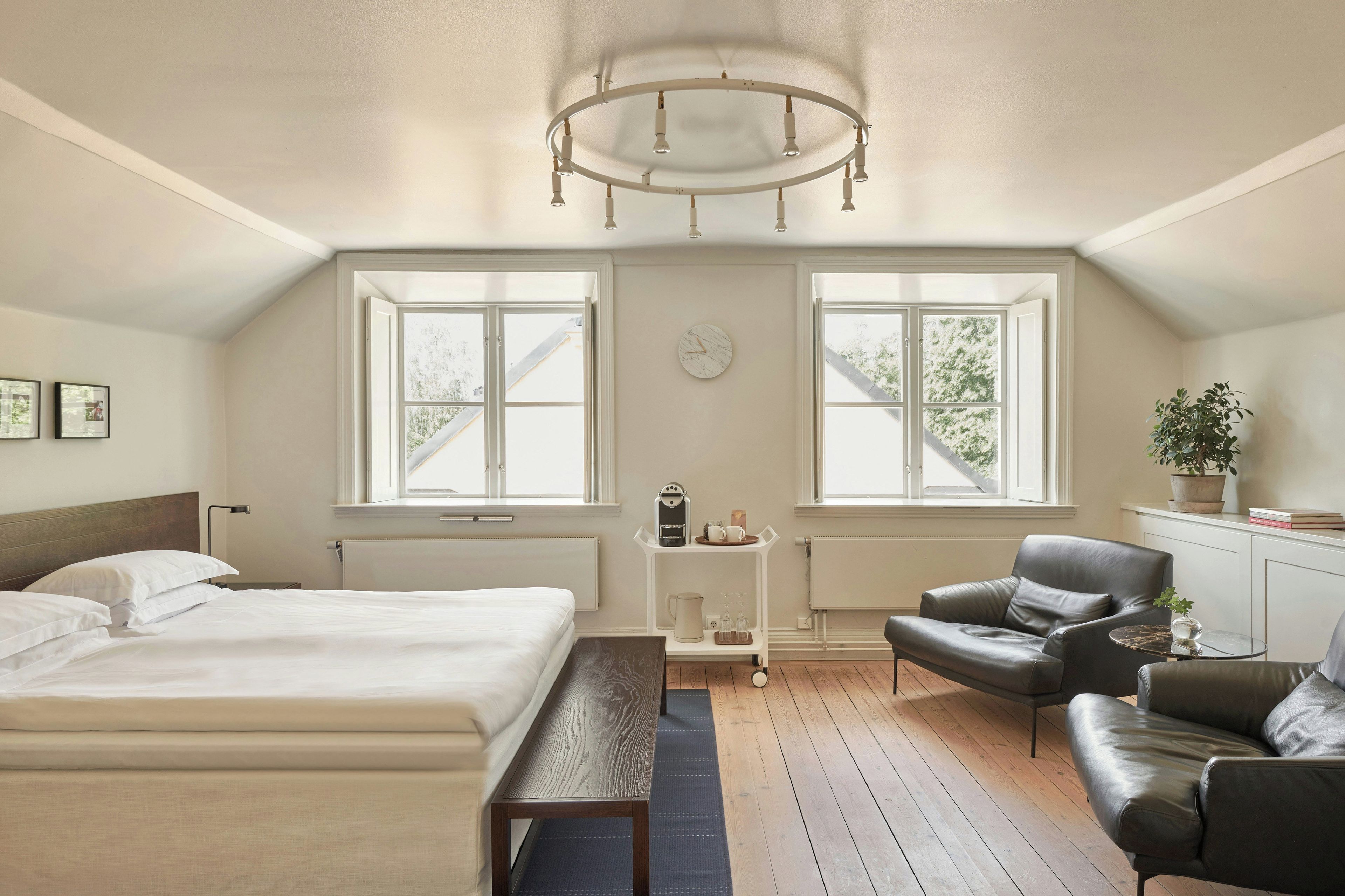 A bedroom with a bed, a desk, a chair, a window, and a plant.