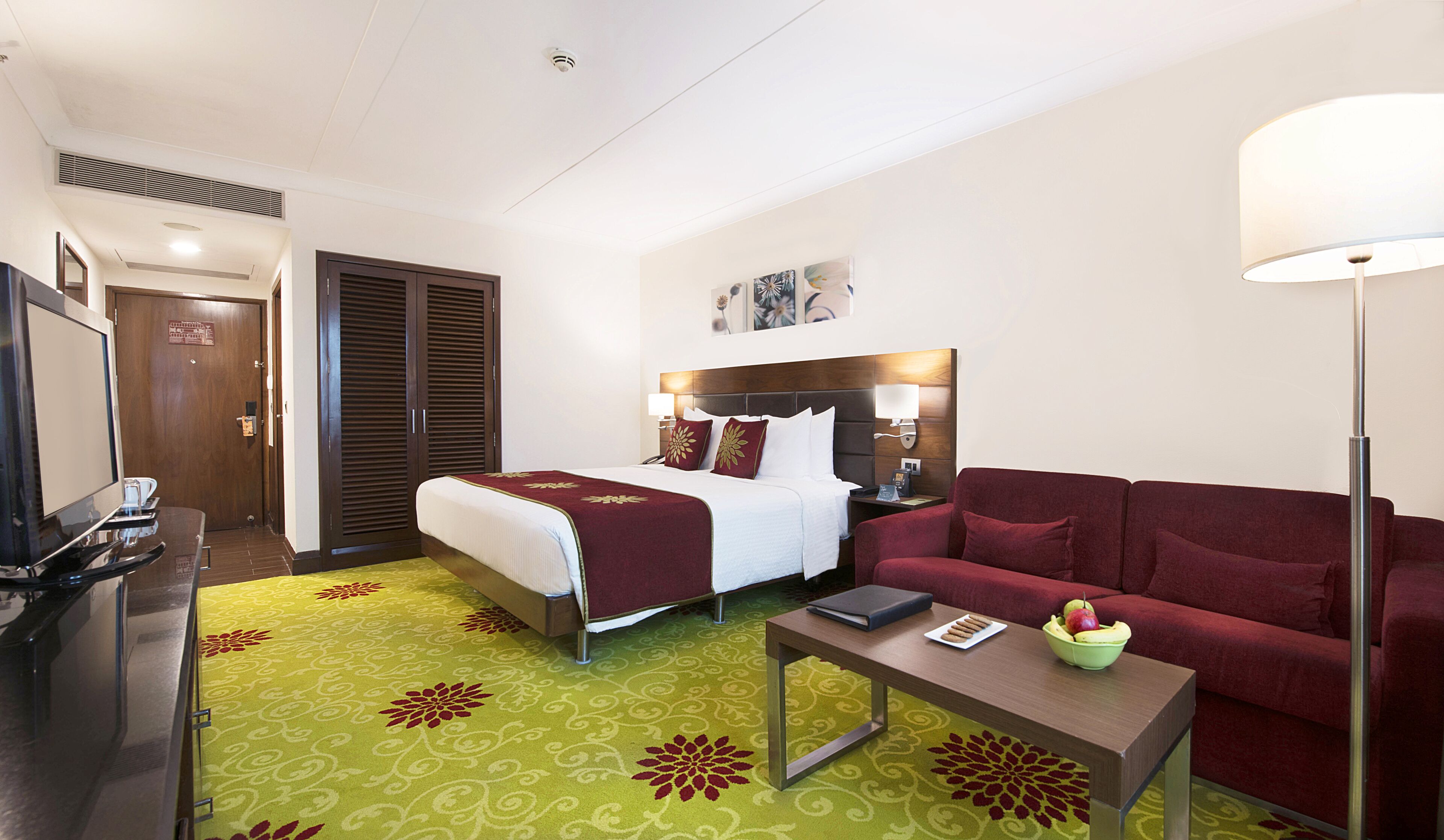 A hotel room with a bed, a sofa, a desk, a TV, and a lamp.