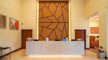 Un mostrador de recepción con un panel de madera geométrico, una silla moderna y una obra enmarcada en la pared.