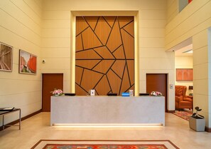 A reception desk with a geometric wooden panel, a modern chair, and a framed artwork on the wall. - Hilton Garden Inn New Delhi/Saket (New Delhi)