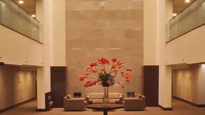 Un hall d’entrée spacieux avec un plafond haut, un arrangement floral central et plusieurs étages visibles à travers des rampes de verre.