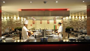 Une cuisine professionnelle équipée de deux cuisiniers qui préparent les plats, avec des appareils en acier inoxydable et un mur de crédence en pierre.