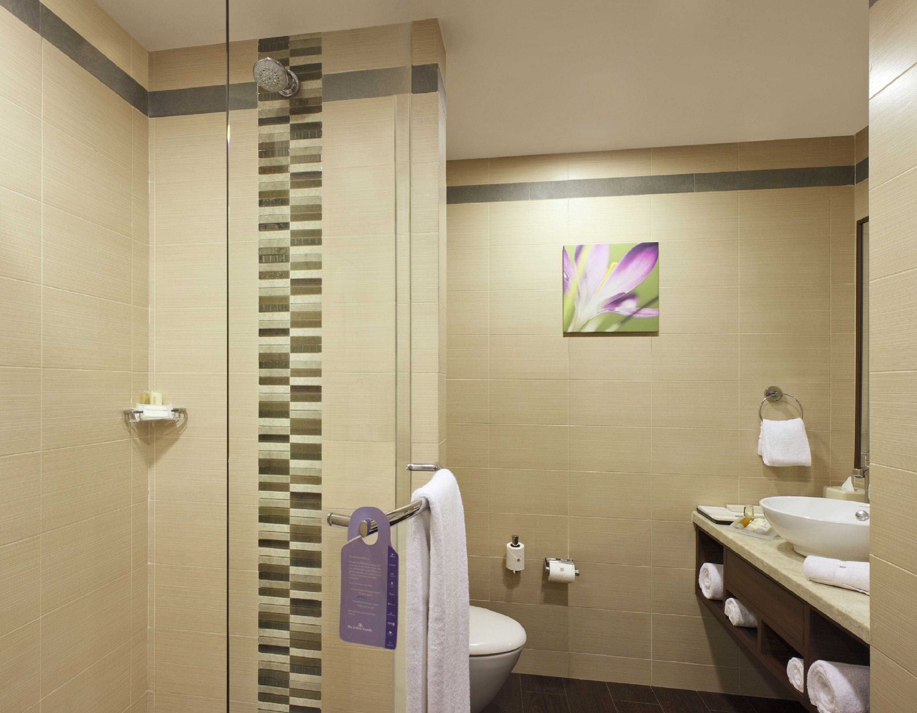 Een moderne badkamer met een douchecabine van glas, een toilet, een wastafel met spiegel en een handdoekrek.