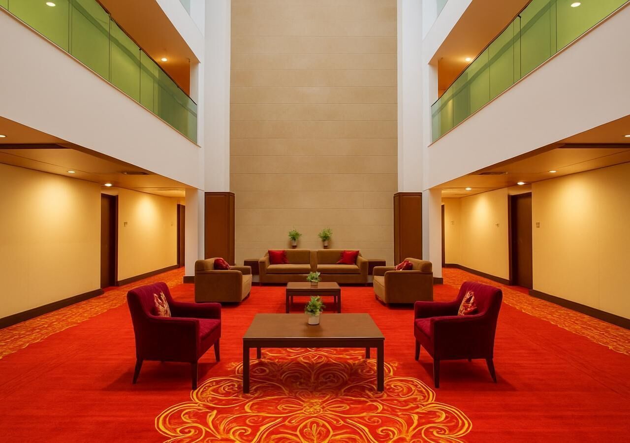 A hotel lobby with a red carpet, a central table with a plant, and seating on either side.