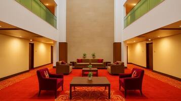 A hotel lobby with a red carpet, a central table with a plant, and seating on either side.