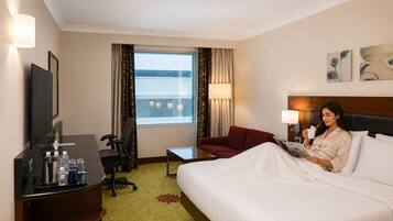 A hotel room with a bed, a desk with a chair, a TV, and a window with curtains.