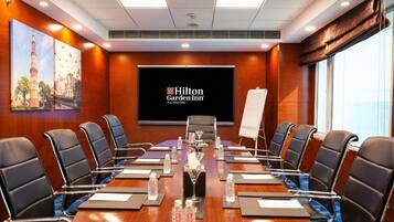 A conference room with a long table, black chairs, water bottles, and a Hilton Garden Inn sign.