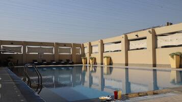 A swimming pool with lounge chairs and potted plants, surrounded by a beige building with large windows.