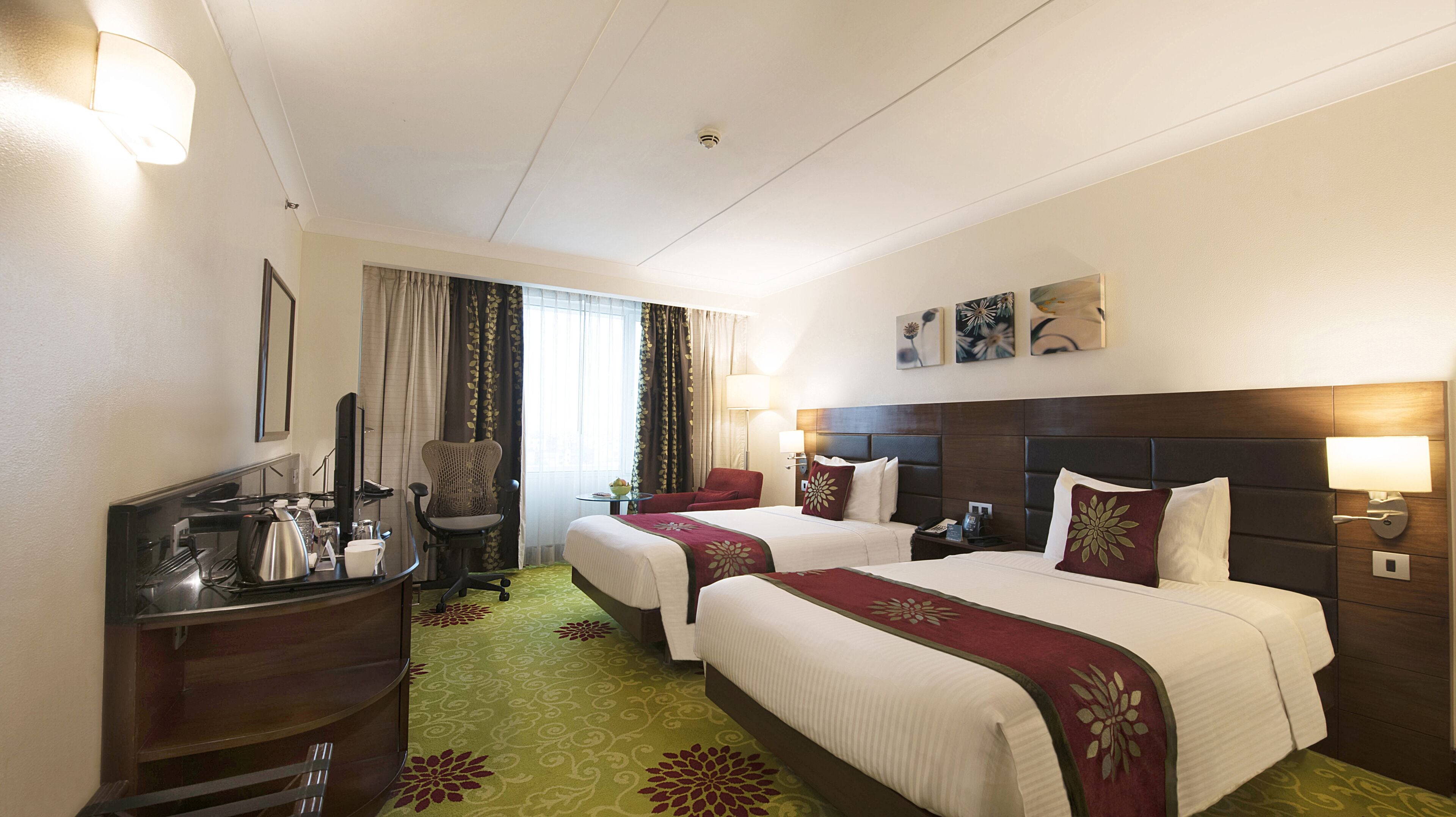 A hotel room with two beds, a desk, a chair, a television, and a window with curtains.