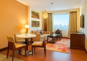 A hotel room with a dining area, a sofa, a TV, and a large window with a city view. - Hilton Garden Inn New Delhi/Saket (New Delhi)