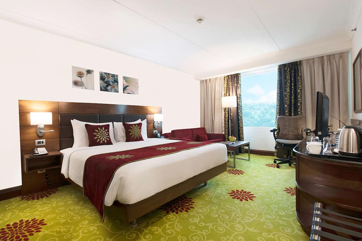 A hotel room with a large bed, a desk with a chair, a television, and a window with curtains.