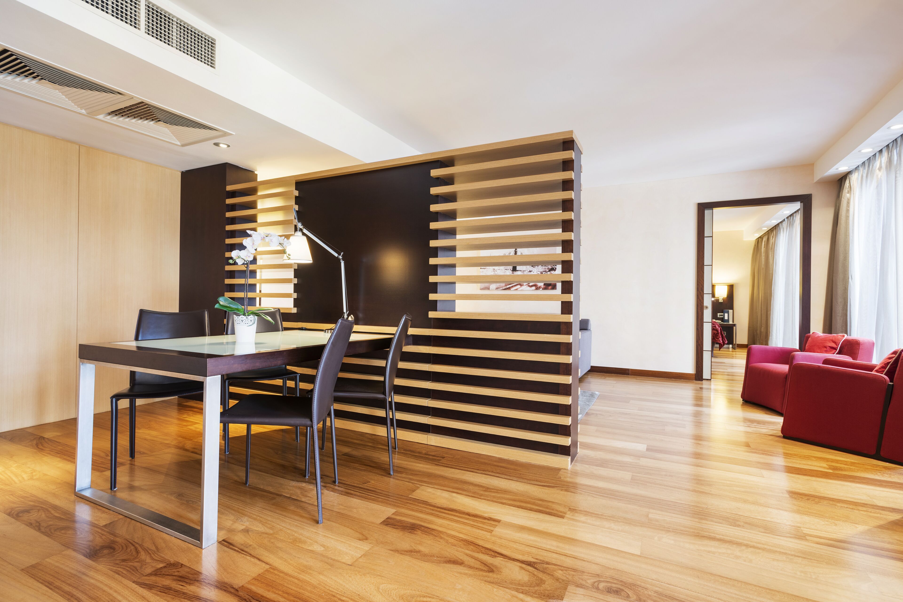 A modern hotel room with a dining area, a red sofa, and a wooden partition.