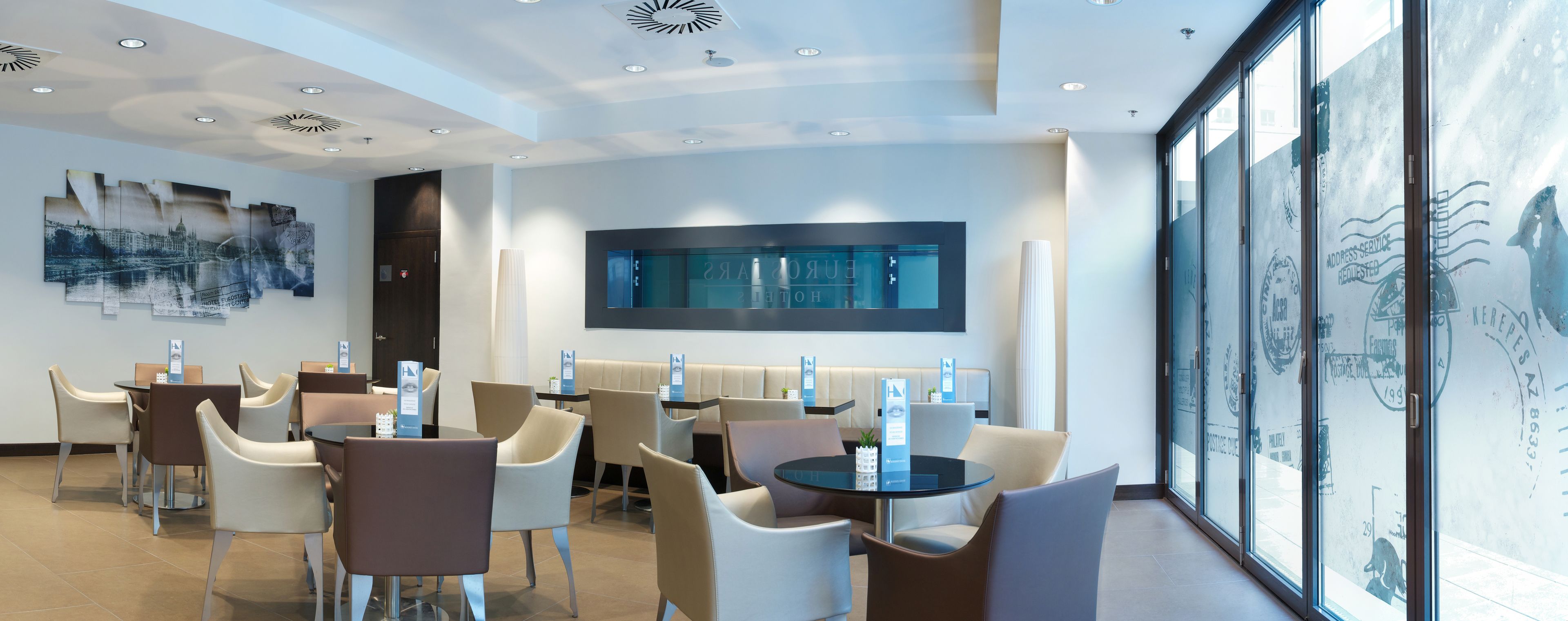 Un hall d’hôtel doté d’un espace salon, d’un grand téléviseur fixé au mur et d’une œuvre d’art représentant un paysage urbain.
