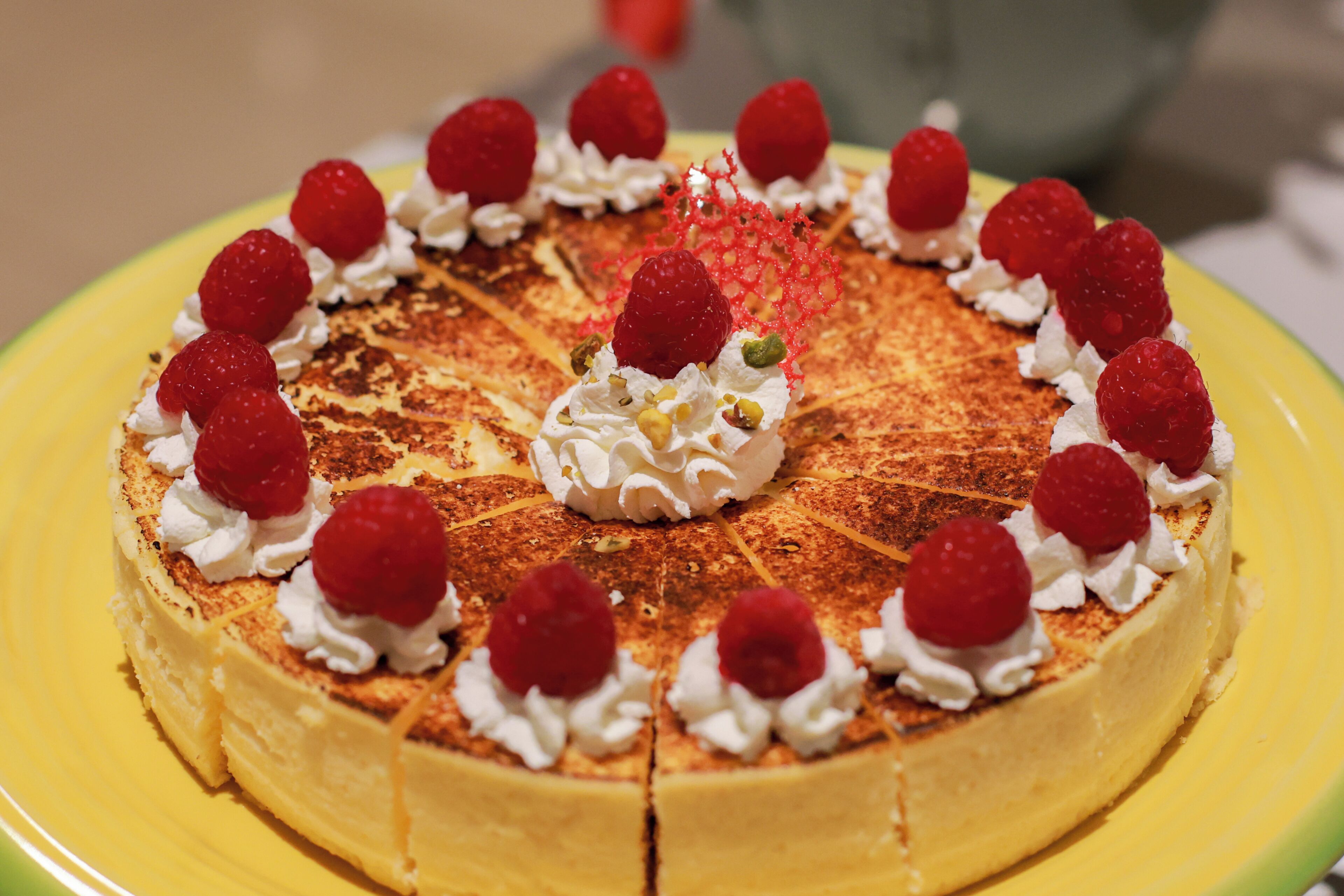 Un pastel redondo con crema y frambuesas sobre un plato amarillo.