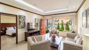Habitación de hotel con cama, televisor, sofá, mesa de centro y vista a la piscina y árboles.