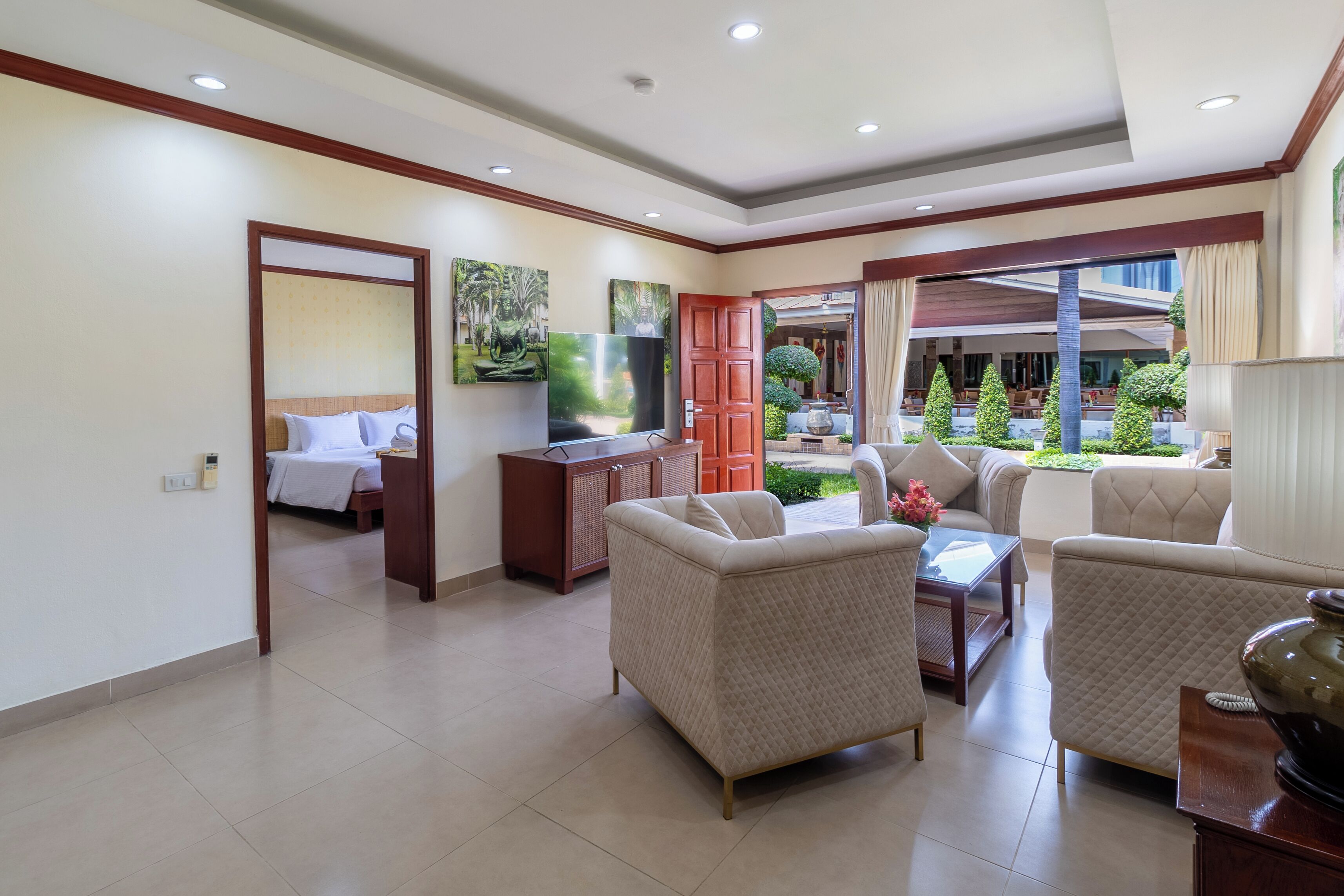 A spacious hotel room with a large bed, a seating area with sofas, a TV, and a view of the garden.