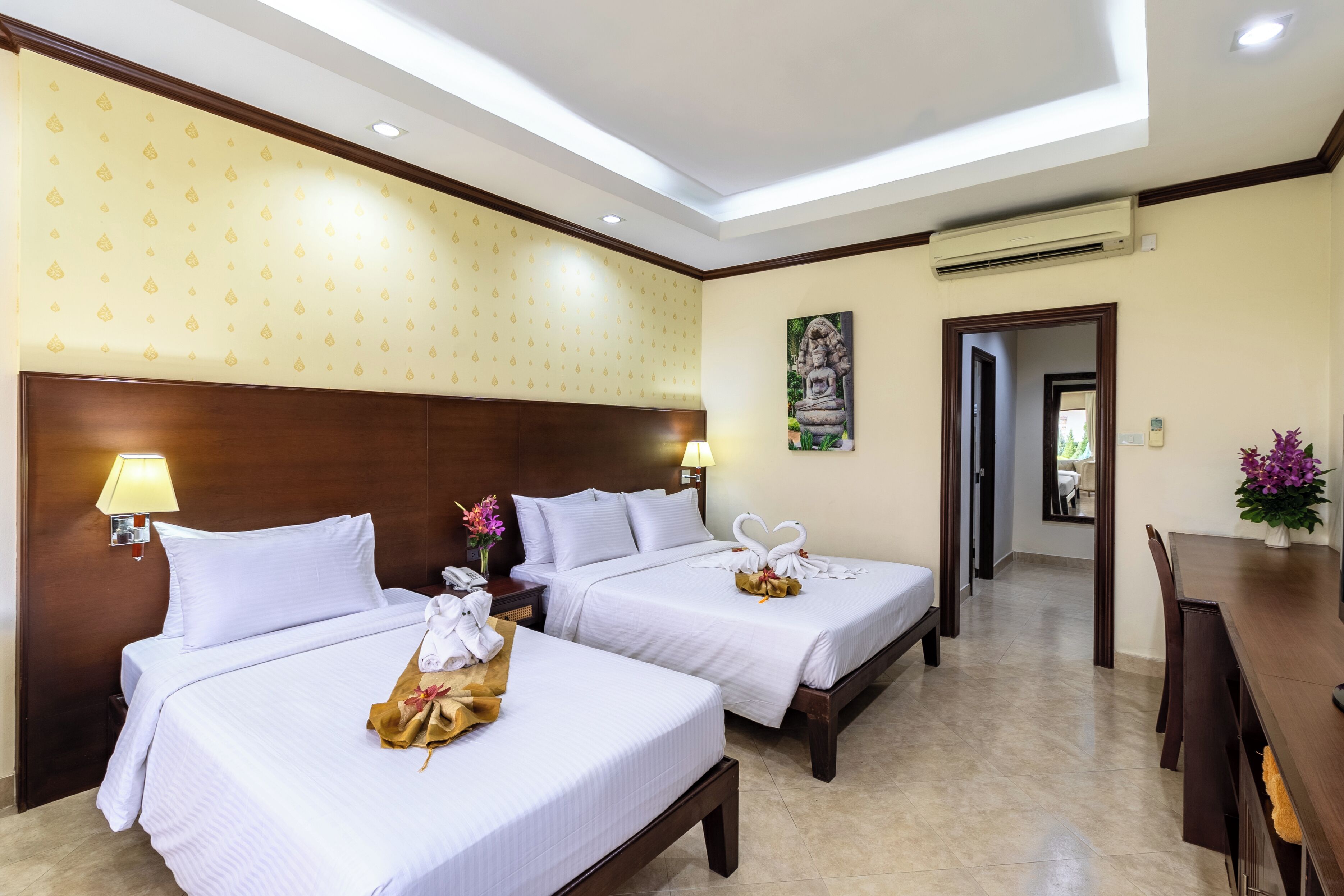 Habitación de hotel con dos camas, una mesa de comedor y una estatua en la pared.