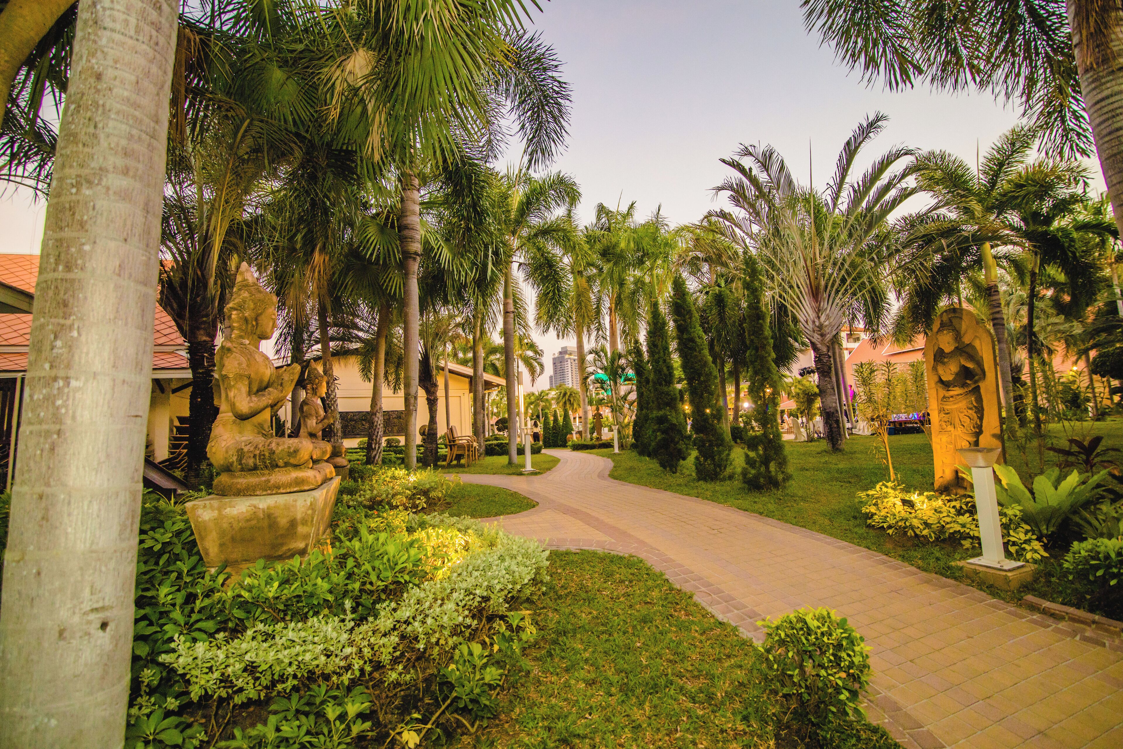 A pathway flanked by palm trees and greenery, leading to a building with a red roof.