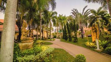 A pathway flanked by palm trees and greenery, leading to a building with a red roof.