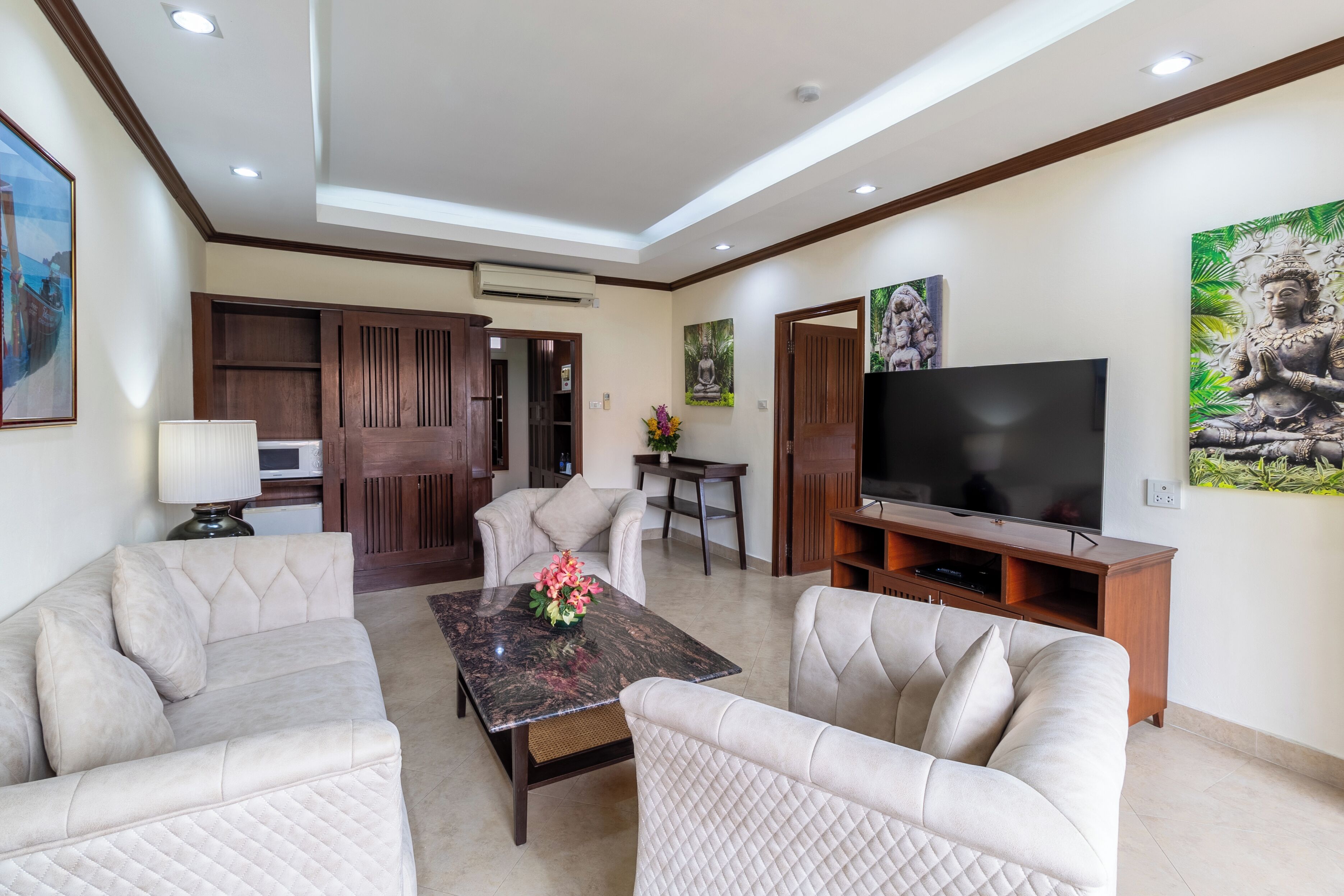 Una sala de estar moderna con una televisión de pantalla plana, dos sofás, una mesa de centro con flores, armarios de madera y obras de arte en las paredes.