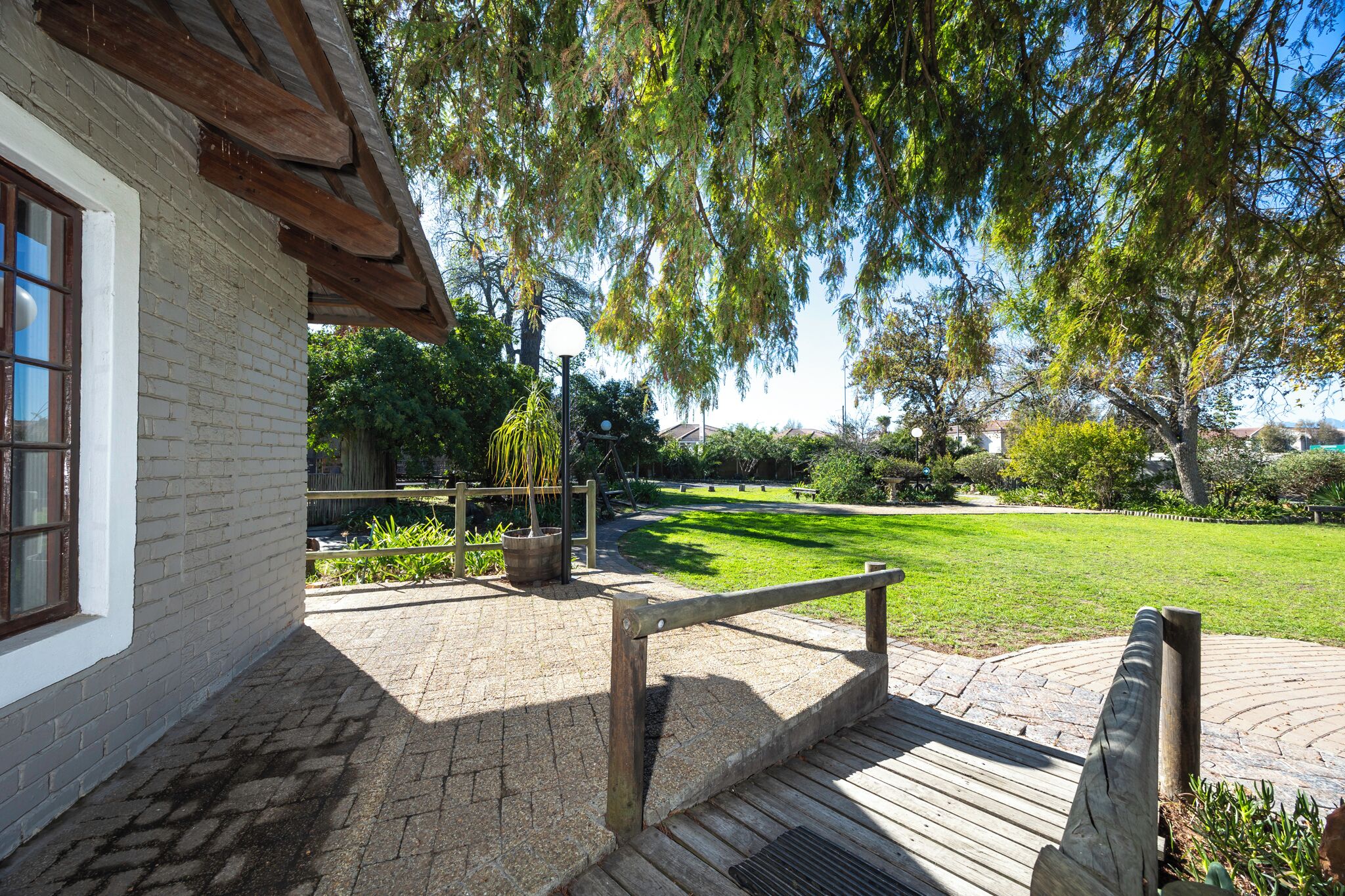 A paved pathway leading to a building with a white facade and a wooden deck.