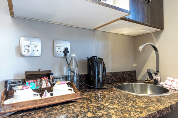 A kitchen with granite countertops, a stainless steel sink, a coffee maker, a kettle, and a tray with breakfast items. - Ruslamere Hotel & Conference Centre (Cape Town)
