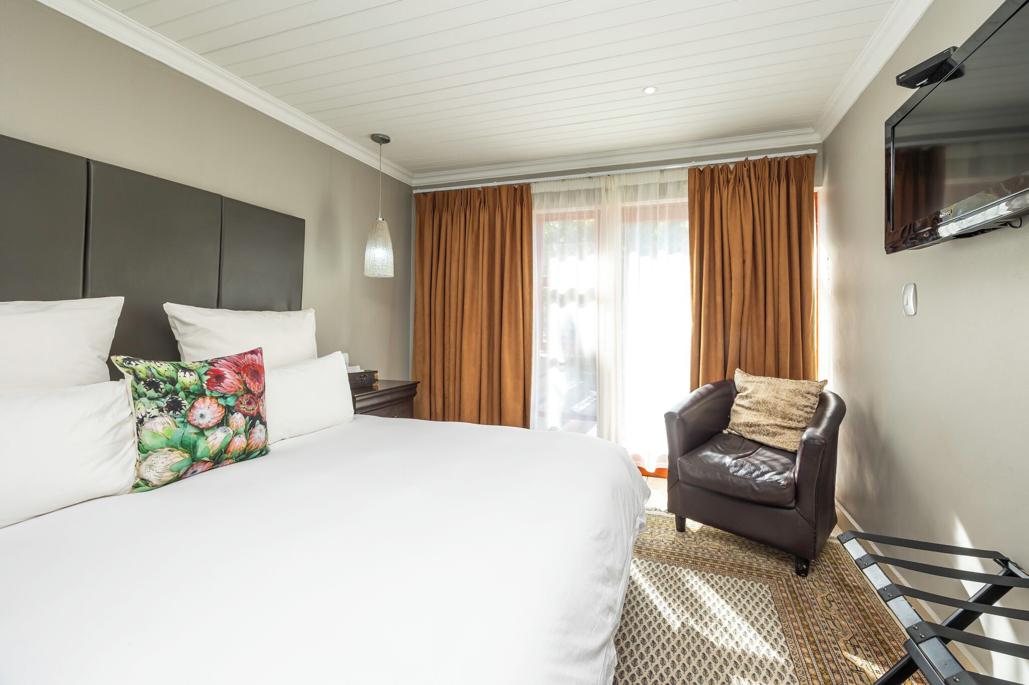 A hotel room with a bed, a TV, a chair, and a window with curtains.